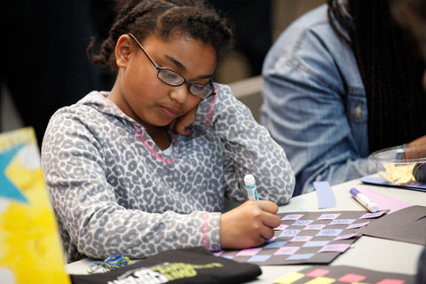 A focused young woman drawing with a marker at the craft table.