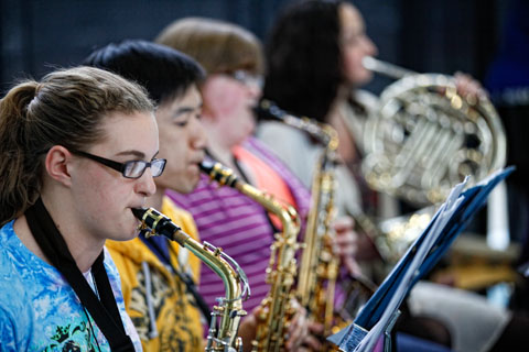 Three students playing saxophones next to another student playing a French horn.