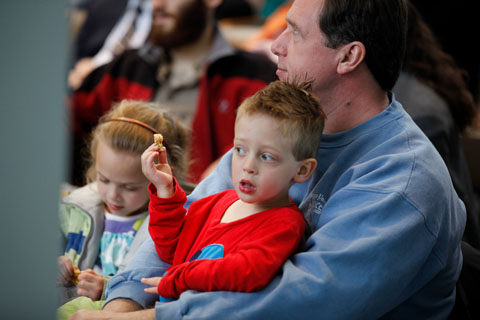 An adult sits with a child on his lap while another child sits next to him