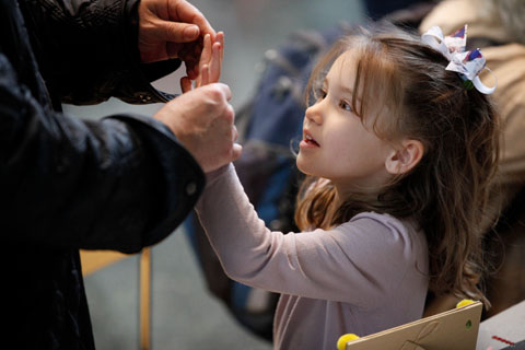 A young girl with a bow in her hair getting help to remove paint from her hand.