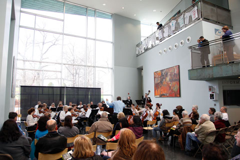 Attendees watching an orchestral performance in front of a large window at the Shapiro Campus Center Atrium.