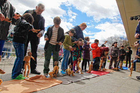 Festival attendees in a line, each attempting to manipulating a marionette with younger attendees getting help from adults.