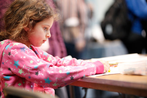 A young, focused girl coloring with a yellow crayon.