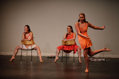 Three young ladies in colorful and coordinated dresses performing on stage.