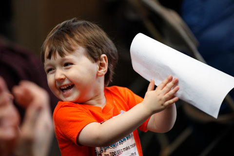 A happy youngster smiling brightly while clapping with a paper on one hand.