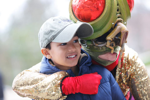 A young smiling man being hugged by someone in a red-eyed bug costume.
