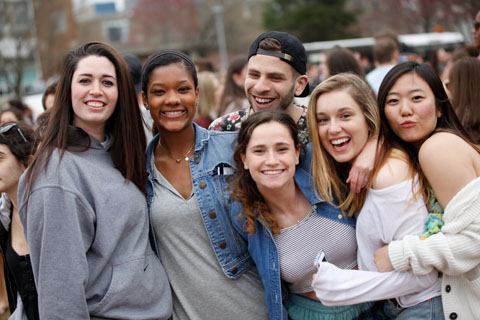 A small bevy of smiling students in a group embrace while posing for the camera.
