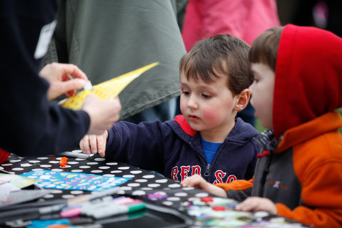 A young child grabbing for a white sticker from a table full of sheets of stickers.