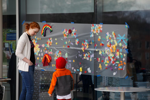A young child stands with a red-haired woman next to a decorated board.