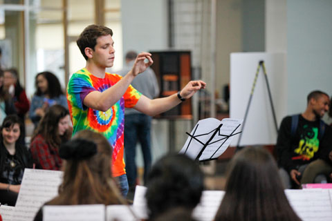 A conductor in a tie-dyed shirt leads the orchestra in a performance.