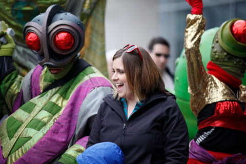 A woman smiling while surrounded by people dressed in red-eyed, full-body costumes.