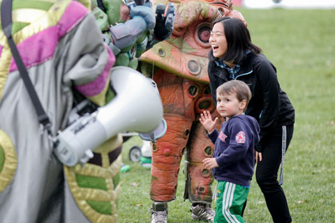 A young, bewildered looking boy with a laughing woman standing amongst a few people dressed in costumes.