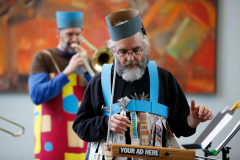 A festively-decorated theremin player with slide trombonists behind him playing along.