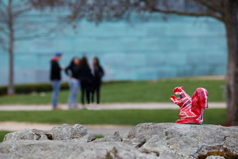 A painted red squirrel sculpture sits on a wall, watching over 4 attendees in the distance.