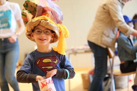 Young boy with a bright, colorful festival hat enjoying popcorn and happily posing for the camera.