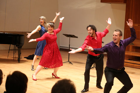 Two men and two women performers singing and dancing on stage.