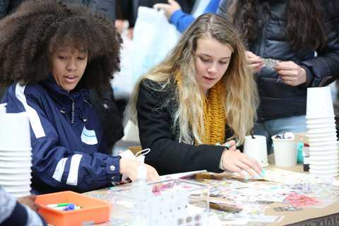 Two young women with stickers sprawled on the table before them, surrounded by other craft supplies.