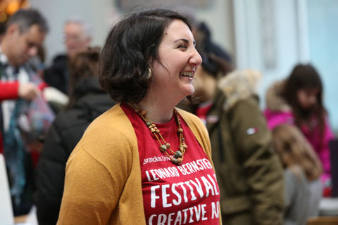 A smiling woman wearing a red Leonard Bernstein Festival of the Creative Arts tee shirt.