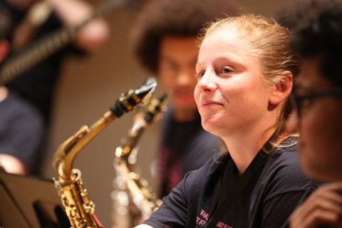 A musician smiling with her saxophone, patiently waiting to begin.