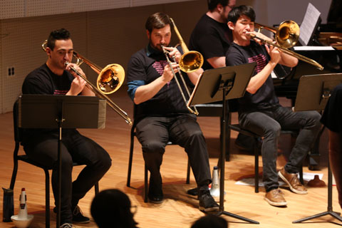 The three men from the horn section of the orchestra playing their trombones.