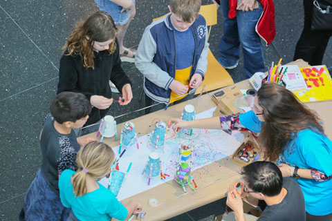 Youngsters modifying cups with markers and battery-powered electronics to make them move and draw on their own.