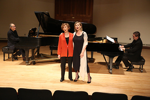Two women singing with piano players in the background.