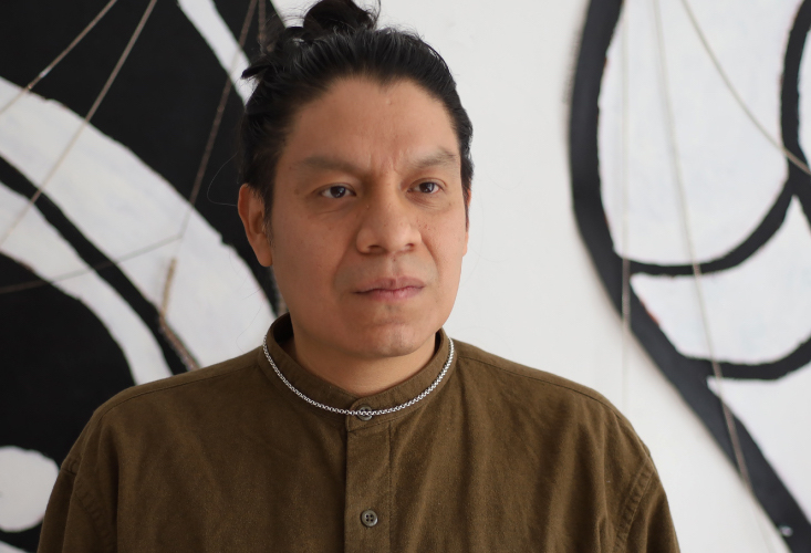 Dark skinned man in brown shirt standing in front of black and white artwork