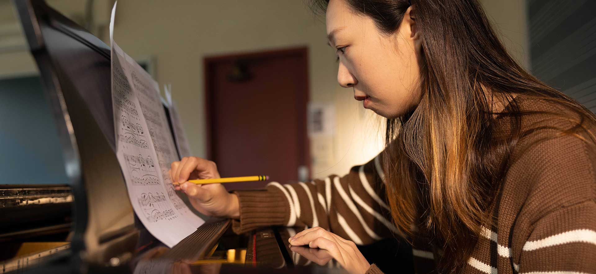 A student sits at a piano annotating music with a pencil