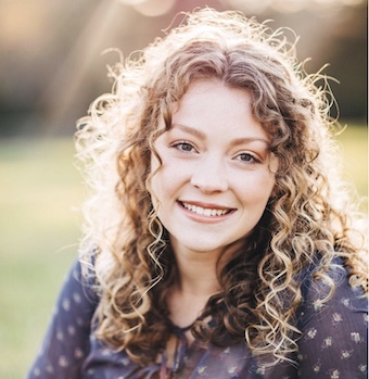 Adah, who has curly hair, is pictured smiling in the sunlight.