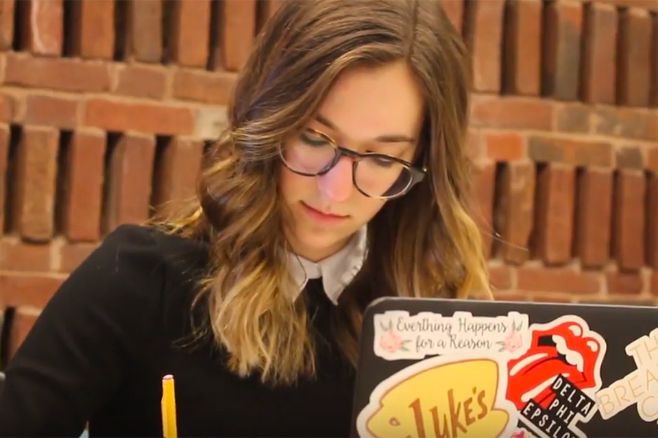 student writing at her desk with open laptop beside her