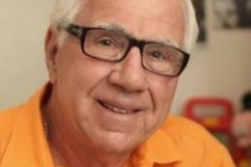 Headshot of Ron Della Chiesa wearing a bright orange shirt