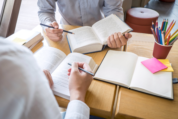 Two people studying with books and a pens