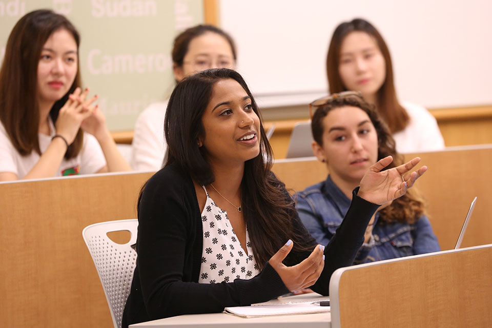 A female student talks, demonstrating with her hands, while other students look on