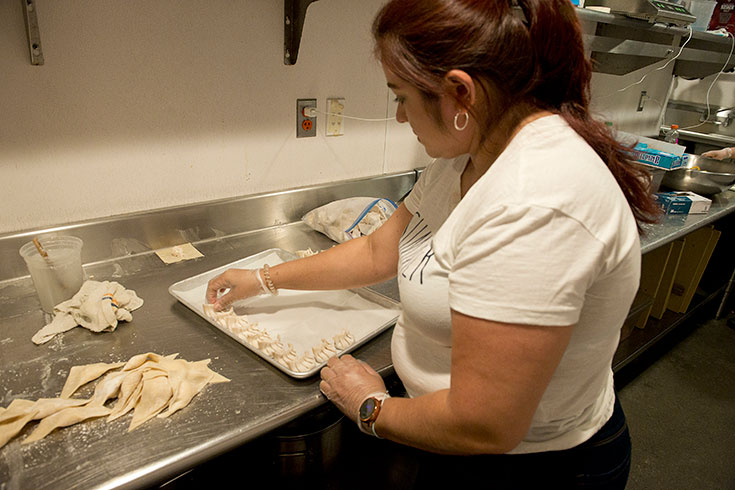 A woman arranges dumplings while cooking in an industrial kitchen