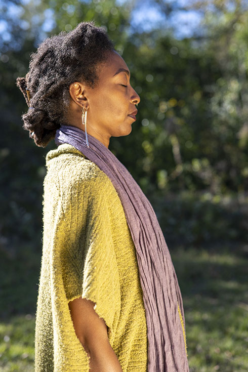 C.Y. stands in profile with her eyes closed, wearing a green sweater and purple scarf