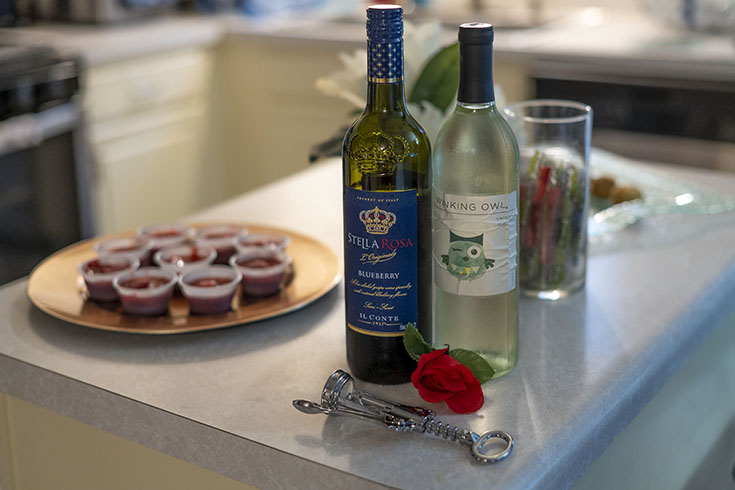 A platter of appetizers, two bottles of wine, and a corkscrew are displayed on a countertop