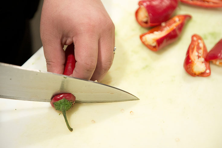 Closeup of someone cutting the top off of a red pepper