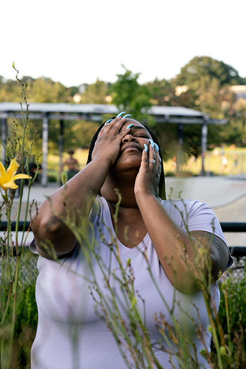 S.P. stands in tall grass, looking to the sky with her hands on her face