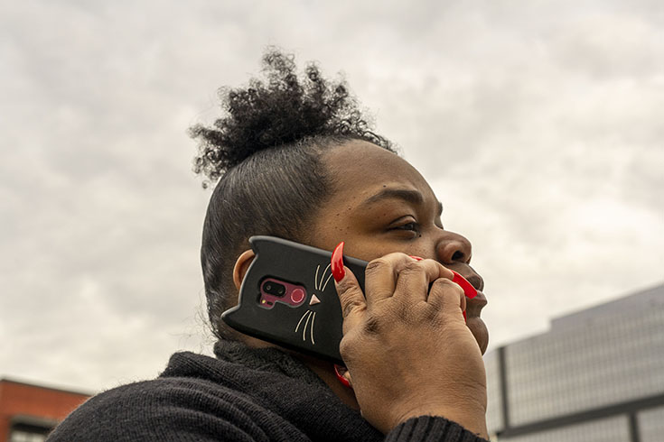 S.P. stands in profile holding her cellphone to her ear. Her fingernails are long and painted red.