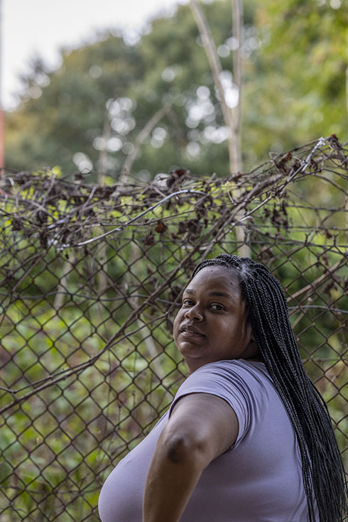 S.P. stands against a wire fence, looking over shoulder at the camera