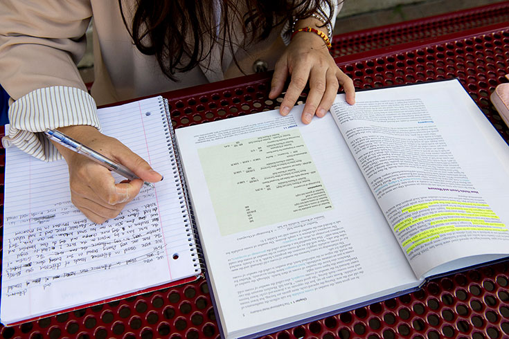 Y.L. holds. a book open while taking notes in a notebook