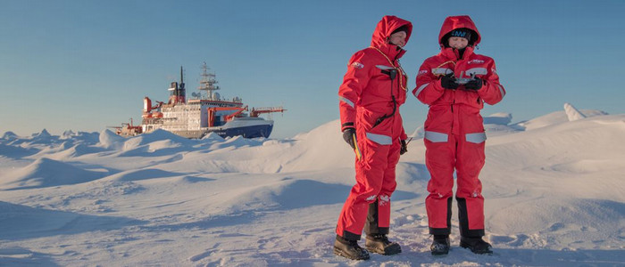 Scientists in orange suits on ice with a ship in the background