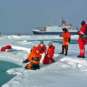 Scientists in orange suits on ice with a hip in the background