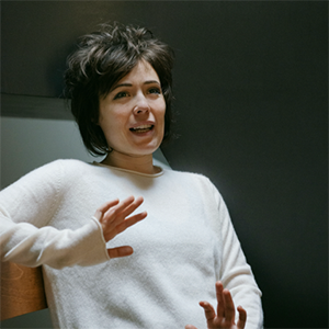 Head shot of Anna Katsman with short black hair in a white sweater speaking