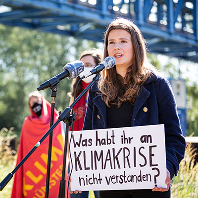 Luisa Neubauer speaking at a climate protest holding a sign.