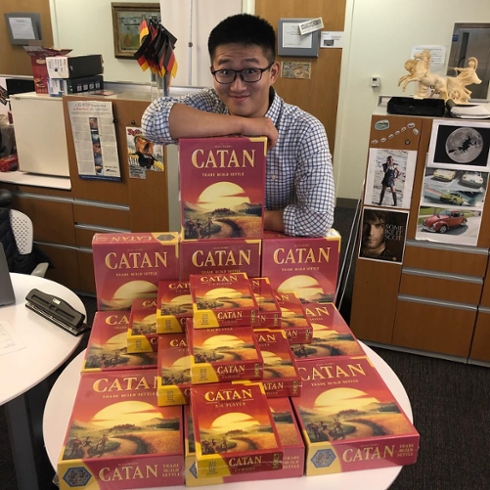 A CGES student employee stands behind a table with many Catan games.