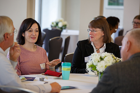 Professor Anjeana Hans and Provost Lisa Lynch in conversation with others at a banquet table.