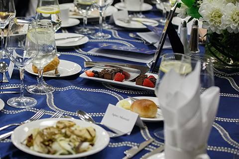 A view of the festive gala dinner place settings with entree, dinner rolls and a dessert plate of chocolate and berries