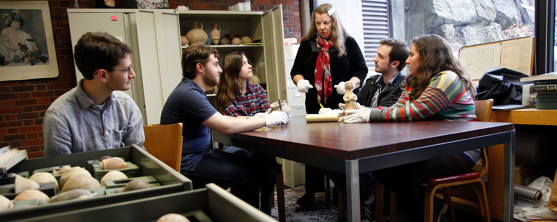 Students listen to a professor while sitting among artifacts