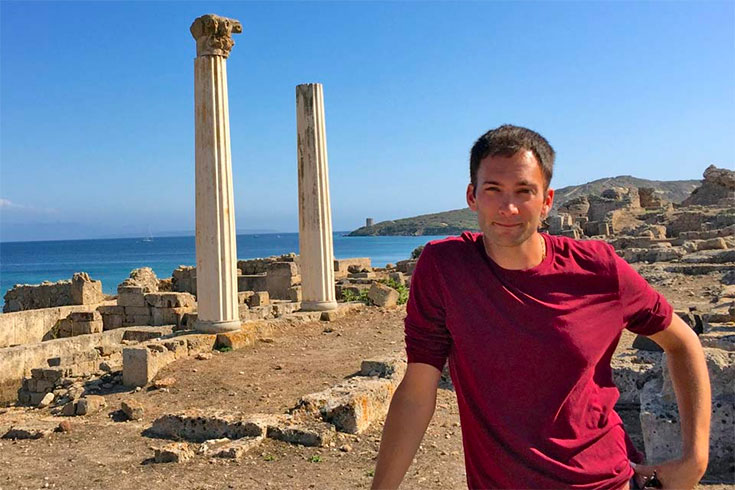 Stephen Guerriero stands in front of ancient columns near the ocean